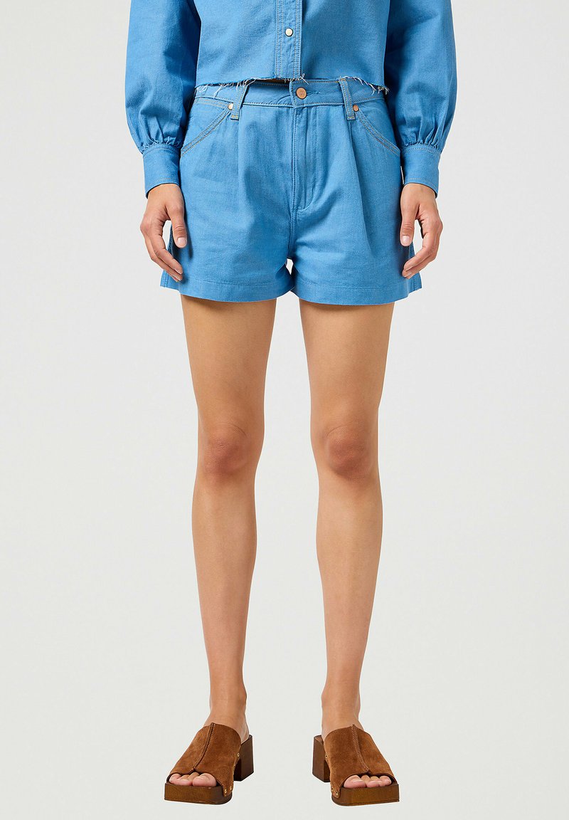 Blå denimshorts med hög midja, med framfickor och rå kant. Matchas med bruna mocka klacksandaler.