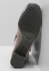 Bota de ante gris con punta redonda, suela de goma texturizada con ranuras para tracción y tacón redondeado. Acentuada con detalles laterales.