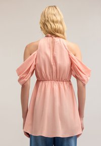 Blusa rosa chiaro a maniche corte con vita arricciata e spalle scoperte. Presenta uno scollo a chiave sul retro con chiusura a fiocco e una morbida texture del tessuto.