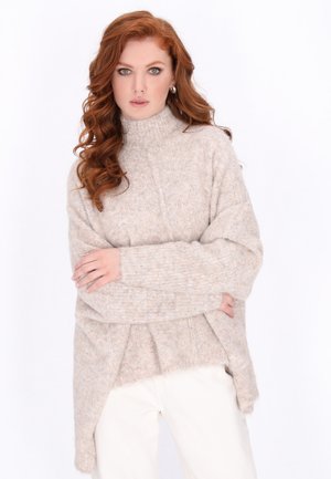 Beige gebreide trui met een hoge nek, verlaagde schouders en zijsplitten. Zachte, gestructureerde stof met een ontspannen, oversized pasvorm.