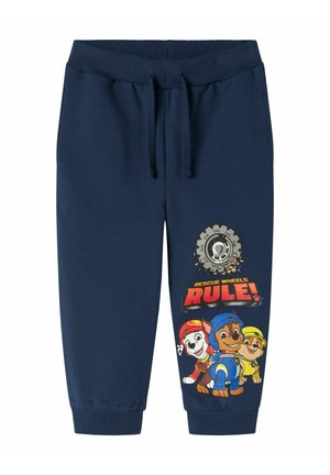 Pantaloni della tuta blu navy con vita elasticizzata, caratterizzati da una grafica di cani cartoon e dal testo "LE RUOTE DI SOCCORSO REGNANO!" in colori vivaci.