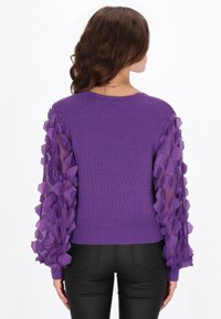 Suéter de punto morado con canalé y mangas abullonadas transparentes adornadas con detalles florales texturizados en tonos morados. Diseño ajustado, con cuello redondo y dobladillo entallado.