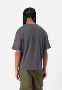Gray cotton short-sleeve t-shirt with a relaxed fit, round neckline, and unfinished hem, paired with loose olive green cargo pants.