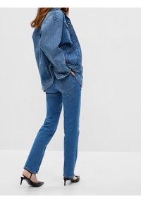 Chaqueta de mezclilla en azul claro con un corte relajado, combinada con unos jeans ajustados azules y sandalias de tacón negras, mostrando una combinación de texturas.