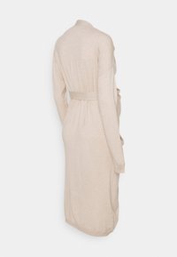 Beige wikkeljurk van zachte stof, met een ceintuur in de taille, lange mouwen en een relaxte pasvorm. Subtiele textuur en gladde afwerking.