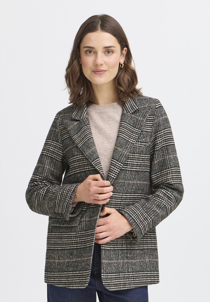Blazer a cuadros en gris, negro y blanco, con solapa clásica y mangas largas. Lleva una sudadera ligera por debajo y presenta un corte relajado.