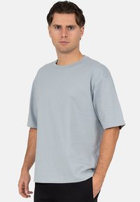 T-shirt bleu clair oversize en tissu doux, col rond, épaules tombantes et manches courtes. Caractérisé par une coupe décontractée et un design simple.