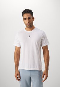 Hvid bomulds T-shirt med korte ærmer, der har et lille sort Jumpman-logo på brystet. Stoffet er glat og let.
