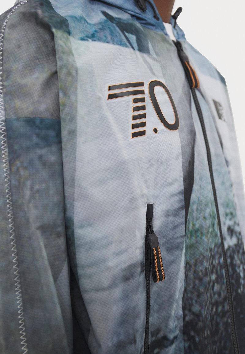 Farbenfrohe Windjacke mit einem fotografischen Landschaftsdesign, ausgestattet mit einem Reißverschluss, verstellbare Kapuze und schwarzen Akzenten.