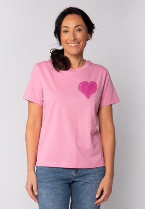 T-shirt en coton rose à manches courtes avec un design de cœur peint sur la poitrine gauche. Coupe décontractée, col rond et texture douce.
