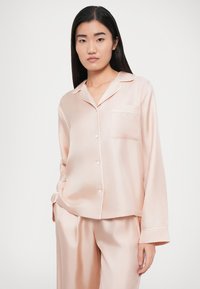 Set di pigiama in raso rosa chiaro con camicia abbottonata dotata di taschino sul petto e piping bianco a contrasto, abbinata a pantaloni a taglio morbido.