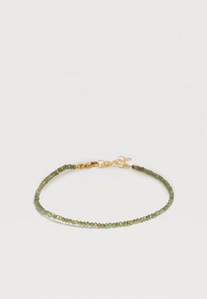 Bracelet délicat avec de petites perles vertes et un fermoir doré avec une chaîne ajustable sur un fond blanc uni.