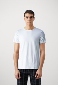 T-shirt en coton bleu clair avec des manches courtes, un col rond et une texture douce. Le modèle le porte avec un pantalon à carreaux noirs.