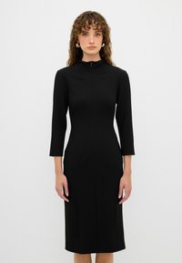 Schwarzes enges Kleid mit hohem Kragen und Dreiviertelärmeln. Glatter Stoff mit einem Reißverschluss vorne und minimalen Nähten, knielang.