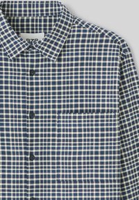 Chemise à carreaux bleu marine et crème, style boutonné avec un col, dotée d'une poche poitrine et d'un motif de tissu texturé.