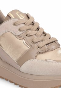 Taupe Sneaker mit gemischten Wildleder- und Satinpaneelen, runden beige Schnürsenkeln und einer Gummisohle mit rutschfesten Profilen, Nahaufnahme von der Vorderseite.