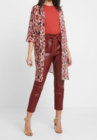 Kimono de estampado floral rojo sobre una blusa roja lisa, combinado con pantalones de imitación cuero burdeos de cintura alta y corte ajustado, y sandalias claras de tacón cúbico.