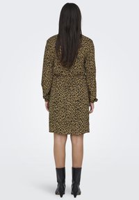Šaty s leopardím vzorom v hnedej a čiernej farbe, látka s jemným leskom, sťahovaný pás, dlhé rukávy, nadkolenná dĺžka, skombinované s čiernymi členkovými čižmami.