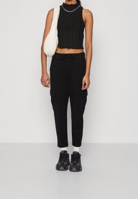 Svart ribbad crop top med en scallop-halsringning, kombinerad med svarta cargobyxor som har fickor och dragsko. Svarta träningsskor med ett camouflage-mönster.