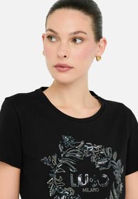 Sort T-shirt med blomstret palietdesign og teksten "LIU·JO MILANO". Korte ærmer og rund halsudskæring fremhæver den tætsiddende stil.
