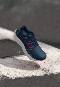 Hardloopschoen in marineblauw met roze accenten, voorzien van een textuur bovenkant, gezepte witte zool en logo-details aan de zijkant.