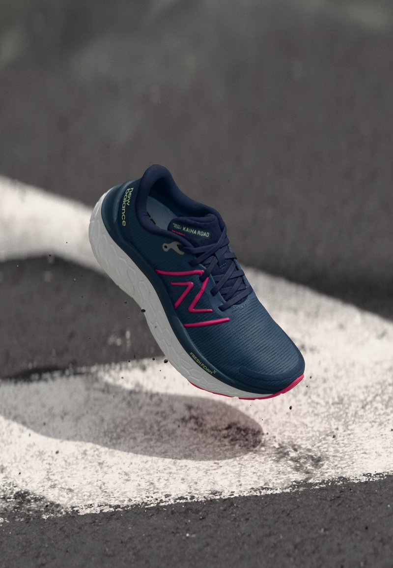 Hardloopschoen in marineblauw met roze accenten, voorzien van een textuur bovenkant, gezepte witte zool en logo-details aan de zijkant.