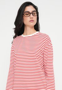 Μακρυμάνικο πουκάμισο με κόκκινες και άσπρες ρίγες, με στρογγυλή λαιμόκοψη, κατασκευασμένο από απαλό ύφασμα, με άνετη εφαρμογή και χαλαρές ραφές στους ώμους.