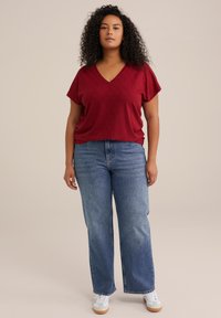 Top V a righe rosso con scollo a V e maniche corte, abbinato a jeans a vita alta blu con gamba dritta e sneakers bianche con suola beige.