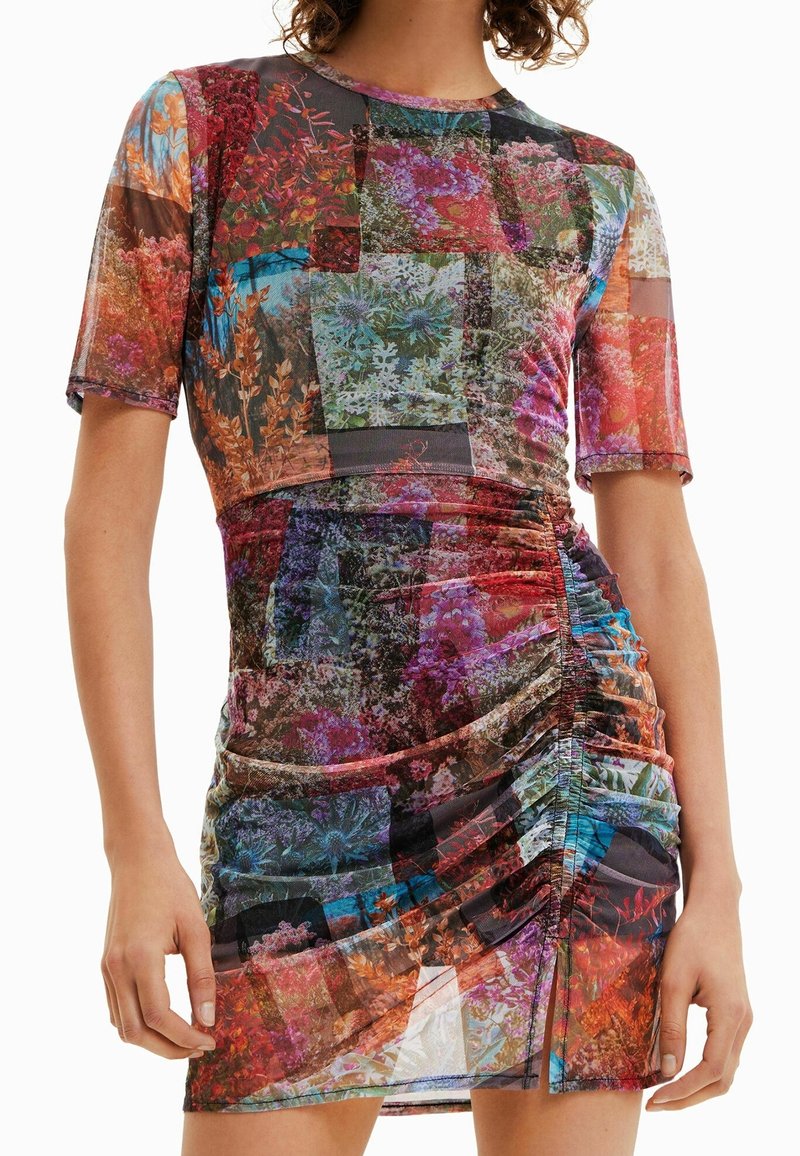 Robe courte patchwork floral froncée avec manches courtes, silhouette ajustée, et mélange de couleurs vives rouge, violet, bleu et orange.