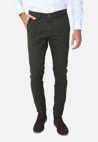Chino verdi in cotone con vestibilità slim, tasche frontali e chiusura con bottone, abbinati a stivali alla caviglia in suede marrone.