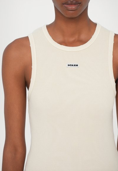 Geribbeld, mouwloos topje in lichtbeige met een ronde hals. Heeft een klein zwart label met "KSUBI" aan de voorkant. Gladde textuur.