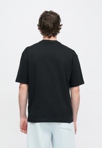 Svart kortermet t-skjorte med rund hals laget av bomull, med et ensfarget design uten mønstre eller pynt, sett bakfra.