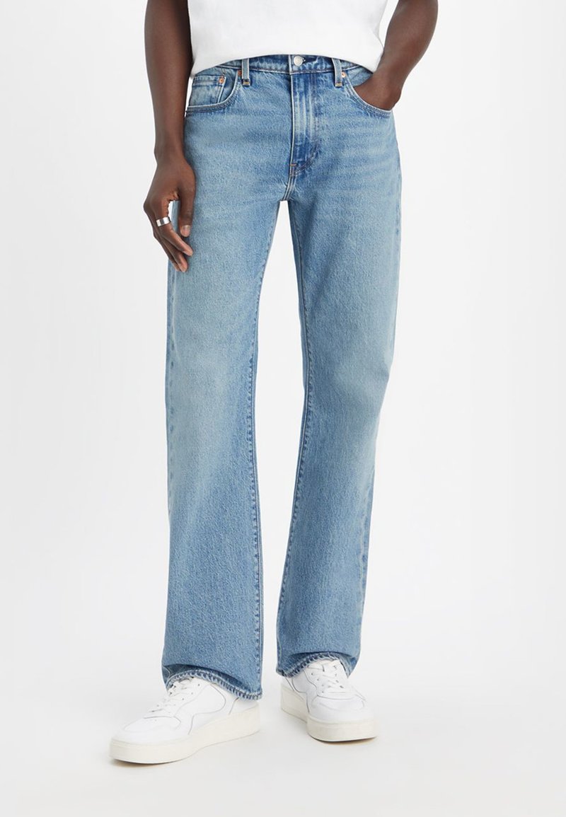 Hellblaue Jeans aus Denim mit geradem Bein, fünf Taschen und einer abgenutzten Textur, kombiniert mit weißen Turnschuhen.