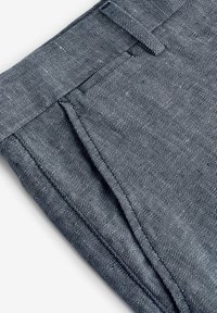 Tissu rayé bleu et blanc, pantalon sur mesure avec un devant plat, taille visible et deux poches latérales, montrant une texture légère.