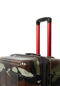 Hård resväska med ett kamouflage-mönster, svart dragkedja och röd utfällbar handtag med texten "BYGGD FÖR ATT MOTSTÅ".