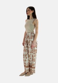 Beige mouwloos topje gecombineerd met wijde broek met een groot bruin bloemmotief en een elastische tailleband. Draag met beige flats.