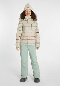 Cremfarbene Schneejacke mit mehrfarbigen Mustern und vorderem Reißverschluss, kombiniert mit hellgrünen Schneehosen. Abgerundet mit einer gestrickten beigen Mütze.