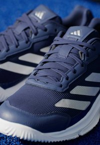 Двойка сини спортни обувки Adidas с бели ивици и текстилна горна част на синя повърхност.