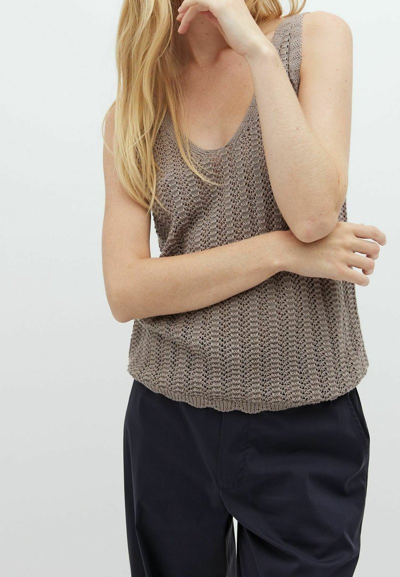 Top in maglia beige con scollo a barca, caratterizzato da un motivo testurizzato e una vestibilità rilassata, abbinato a pantaloni scuri.