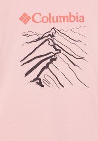 Camiseta de cuello redondo en rosa claro con un gráfico de montaña oscura y el logo de "Columbia" en naranja. Material de algodón con textura suave.
