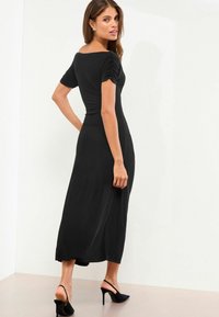 Rochie midi neagră cu mâneci scurte și pliate, croială ajustată pe corp și fustă evazată. Asortată cu tocuri slingback negre. Material neted și elastic.