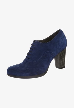Stivaletto in camoscio blu navy con punta arrotondata, design con lacci e dettagli decorativi in stile brogue. Tacco alto spesso e suola texturizzata.
