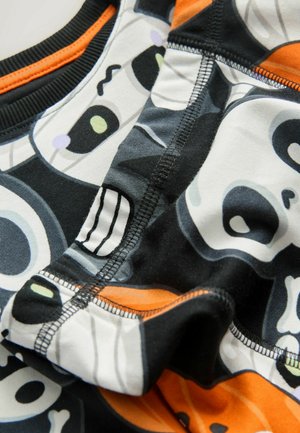 Musterstoff mit schwarz-weißen Totenköpfen und bunten Akzenten. Elastische Ränder mit orangefarbenen Highlights und sichtbaren Nahtdetails.