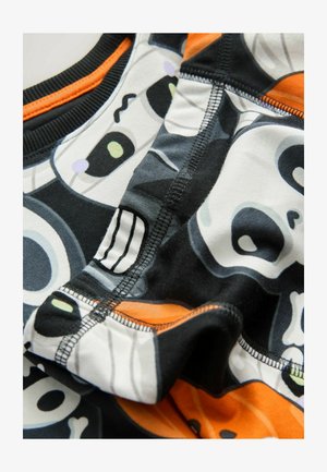 Tessuto stampato con teschi neri e bianchi con accenti colorati. Bordo elastico con dettagli arancioni e cuciture visibili.
