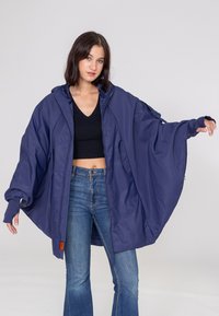 Veste oversize bleu marine en tissu lisse, dotée d'une capuche, de poches latérales et de manches longues avec passe-pouces.