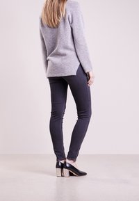 Szary, dziergany sweter z zaokrąglonym dołem, w połączeniu z ciemnymi rurkami i czarnymi szpilkami z srebnymi obcasami w kształcie kostki. Gładka tekstura.