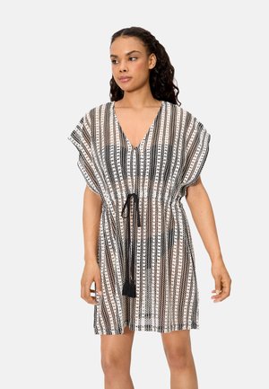 Mujer vistiendo un vestido de patrón a rayas blancas y negras hasta la rodilla, con mangas cortas y un cinturón ajustable con cordón negro en la cintura.