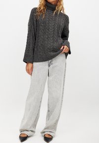 Grå kabelstickad hög hals tröja med lös passform, i kombination med ljusgrå vida jeans och svarta spetsiga ballerinas.