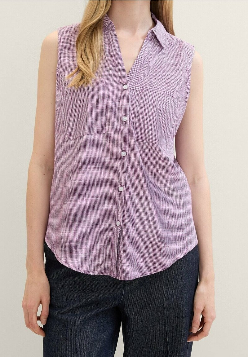 Sleeveless button-up shirt in light purple with a textured check pattern, curved hem, and two front pockets. Paired with dark denim trousers.