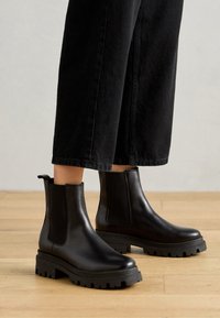 Černé kožené kotníkové boty s elastickými bočními panely, texturovanou gumovou podrážkou, kulatou špičkou a mírně robustním designem.